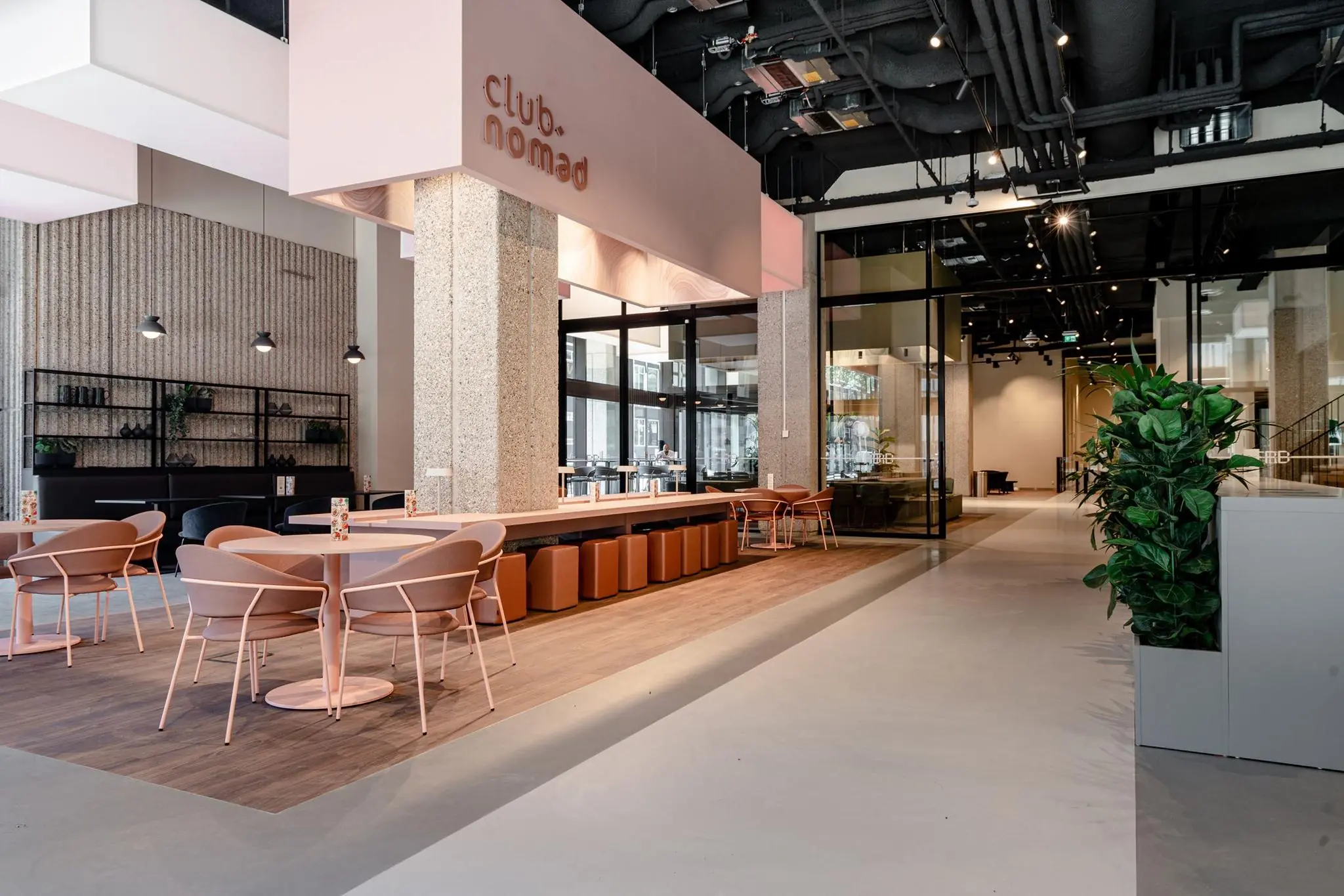 Modern interieur van Club Nomad aan de Aert van Nesstraat met roze zitmeubilair, hoge plafonds en stijlvolle afwerking.